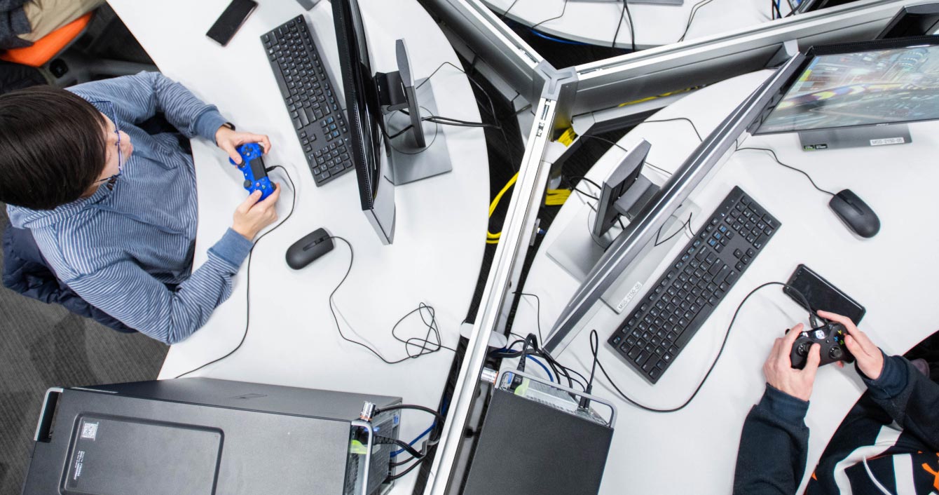 Overhead view of students using game controllers in front of computer monitors.