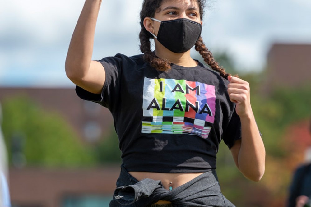 Girl in field with hand raised wearing mask