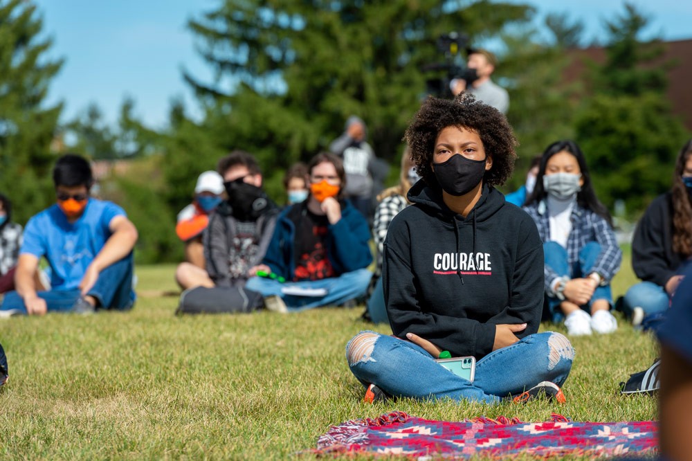 Students sitting in lawn watching presentation wearing masks