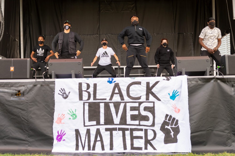 Students dancing on outdoor stage, BLM flag in foreground.