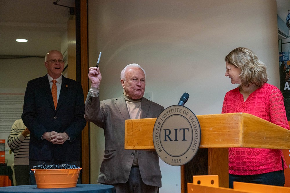 two people standing to the side as a person speaks at a podium.