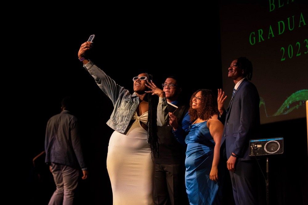 three college students pose for a selfie with another student.