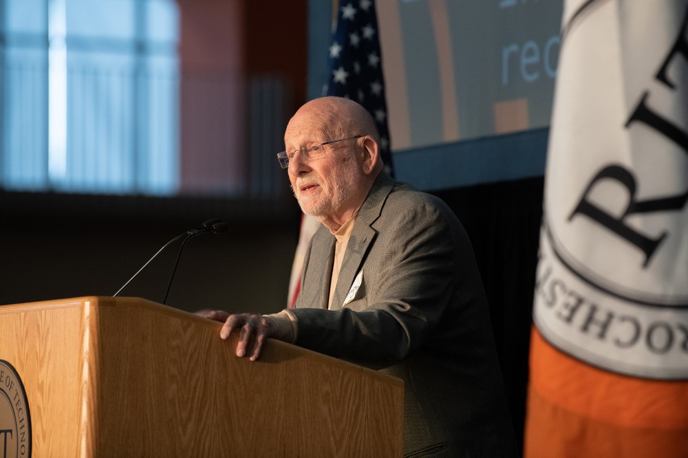 retired professor speaking at a podium.