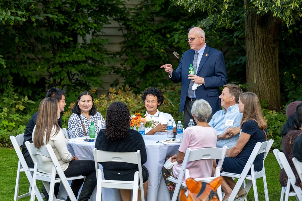 university president talking to a group of college students seated at a banquet table outdoors.