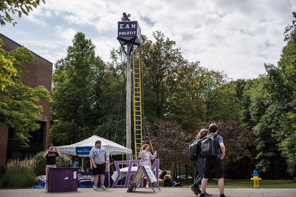 college student sitting in a box at the top of a tall pole structure.