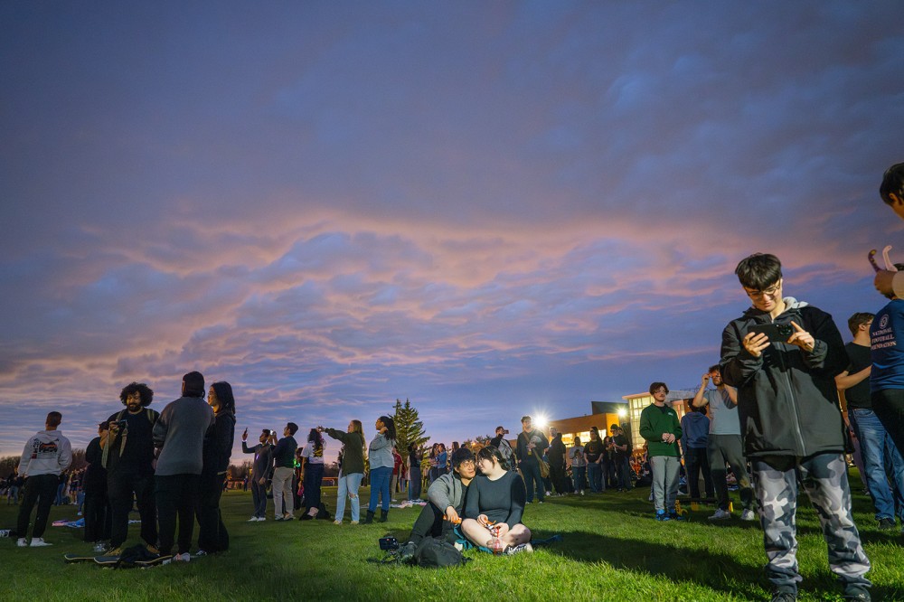 a view of the sky with people sitting and standing watching while it passes.
