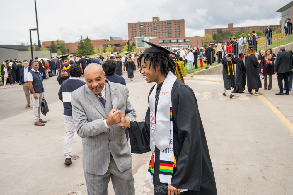 a graduating student accepts a congratulatory handshake outside of the Gordon Field House.