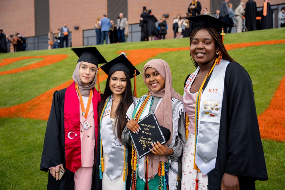 sour students pose in regalia for a photo outside Gordon Field house.