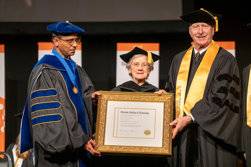 Rita Colwell stands on a stage holding an honorary degree.