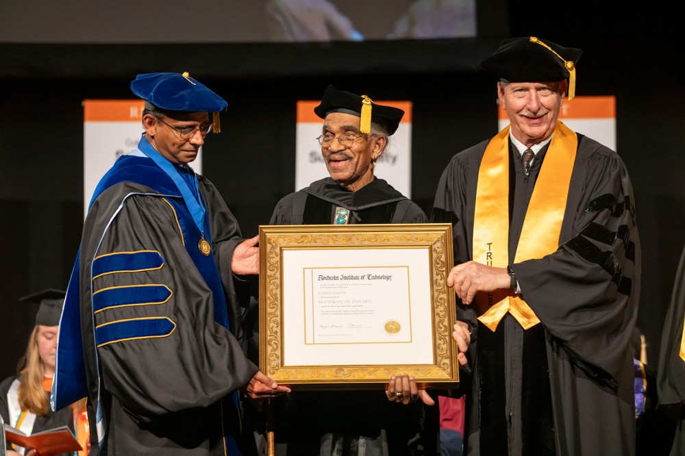 Garth Fagan stands on a stage holding her honorary degree.