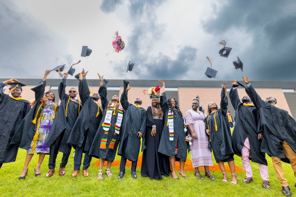 A group of 2024 graduates throw their mortarboards in the air.