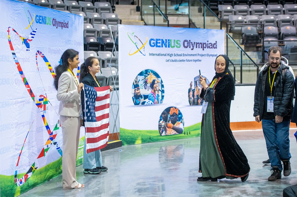 students from another country stand and look at U S students standing with the United Stated flag.
