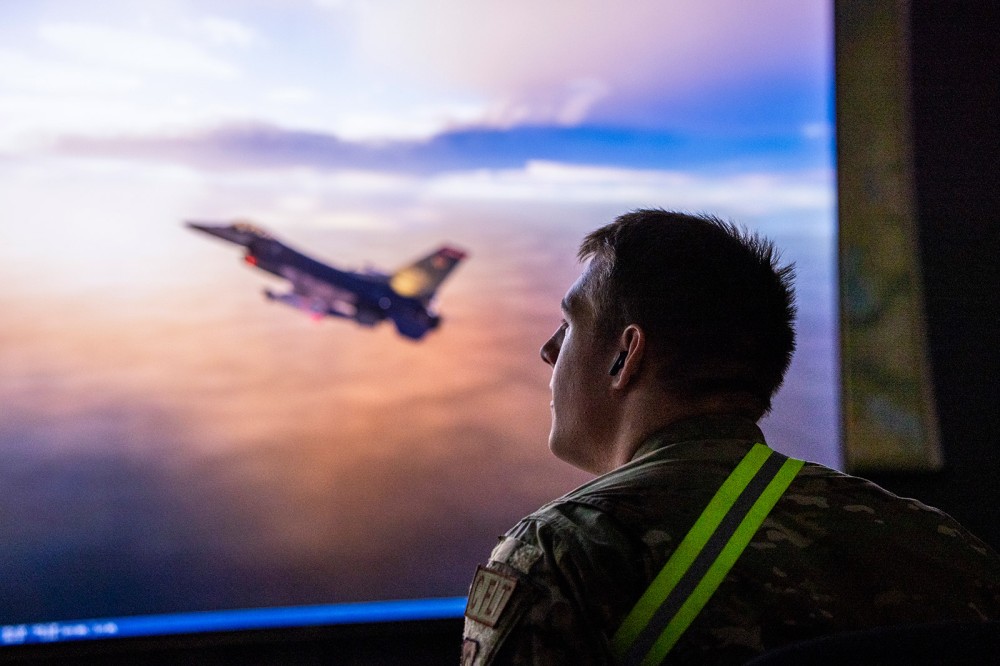 An R O T C cadet looks out a window where a military plane is passing by.