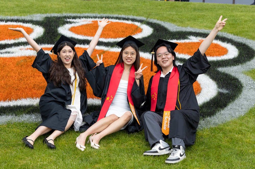 Three students pose for a photo outside the Gordon Field House following commencement.