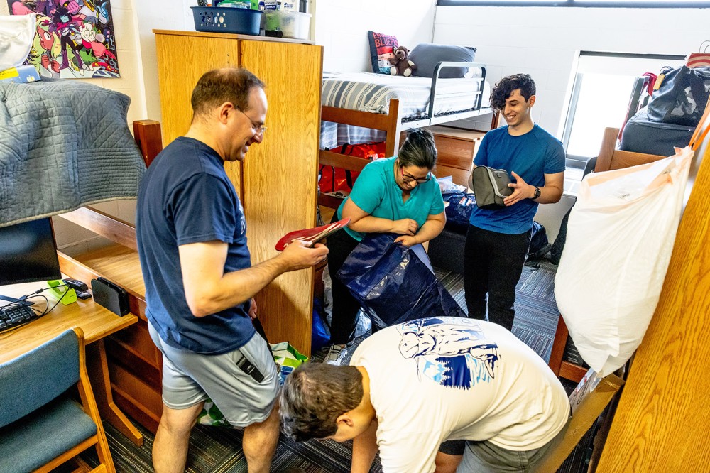 Family unpacks bags and sets up a student’s dorm room with bunk beds and desks.