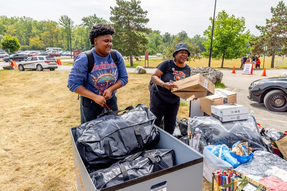 Two people unload bags and boxes during RIT move-in day on a grassy area.