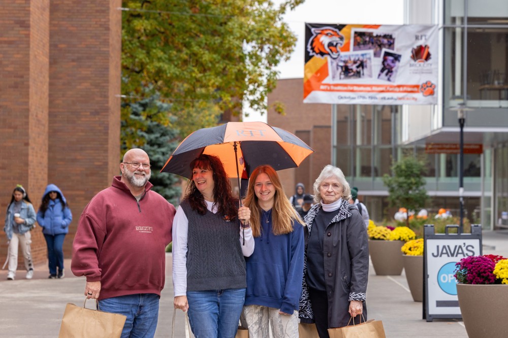 A student stands with her parents and grandmother on campus.