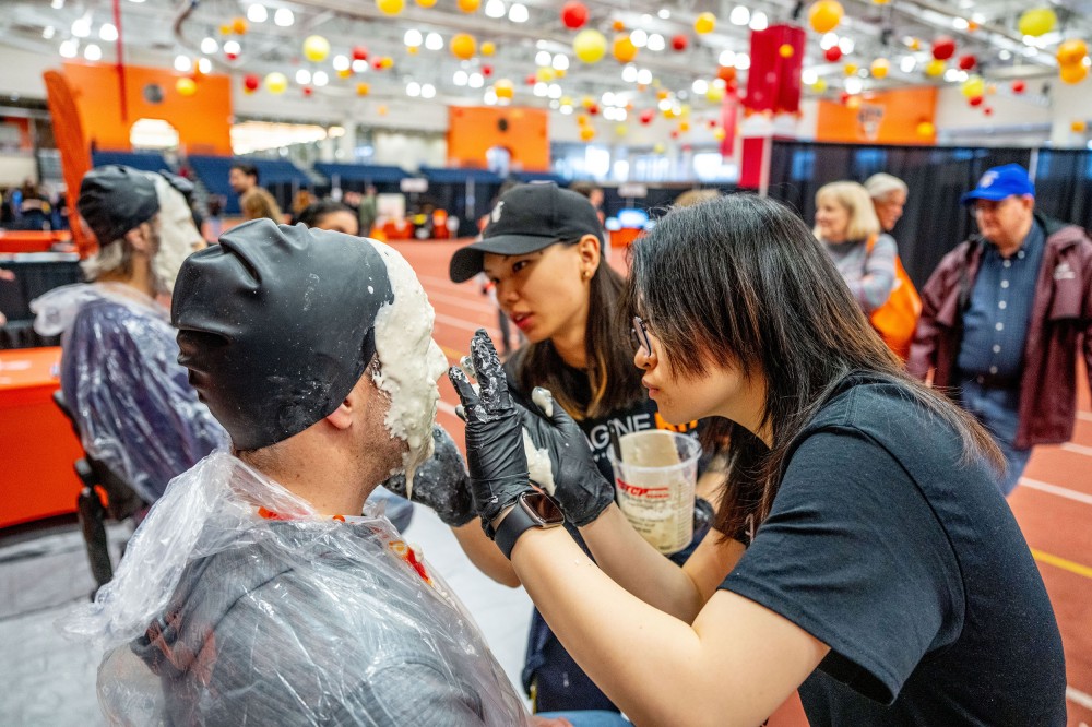An attendee sits while a volunteer applies molding material to their face during a 3D face-portrait activity at Imagine RIT.