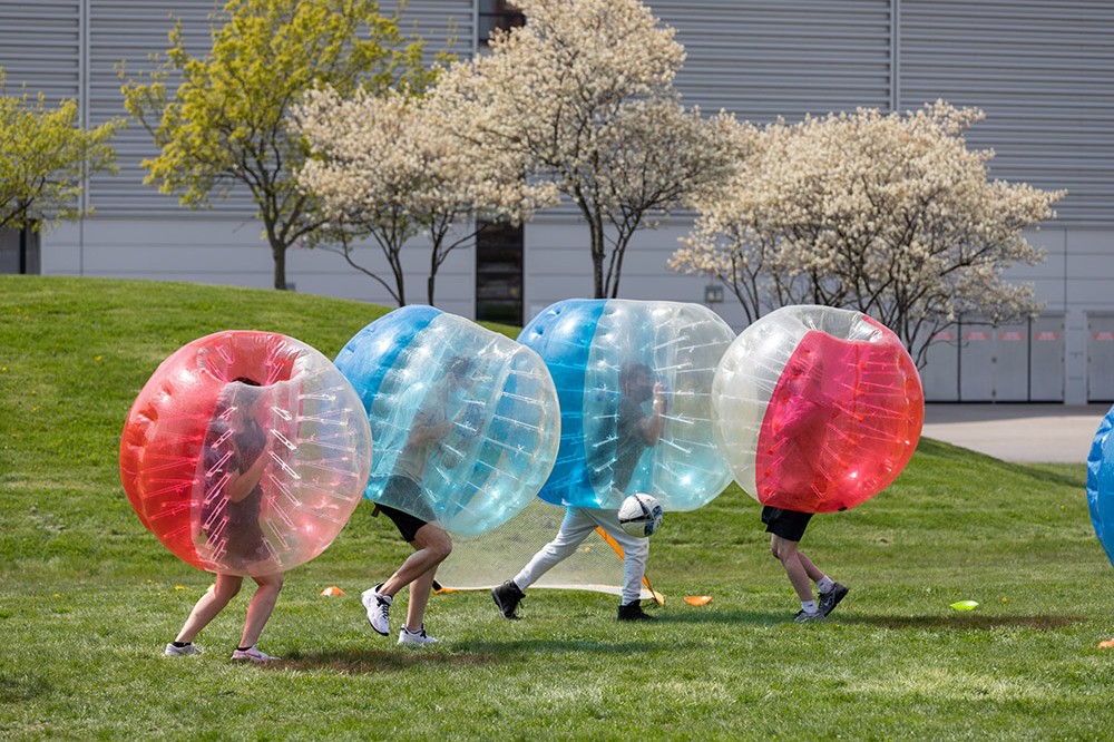 four students wearing giant bubbles playing soccer.