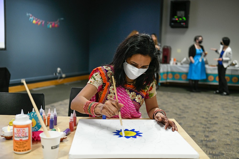 person wearing traditional Indian clothing decorating a poster with glitter.