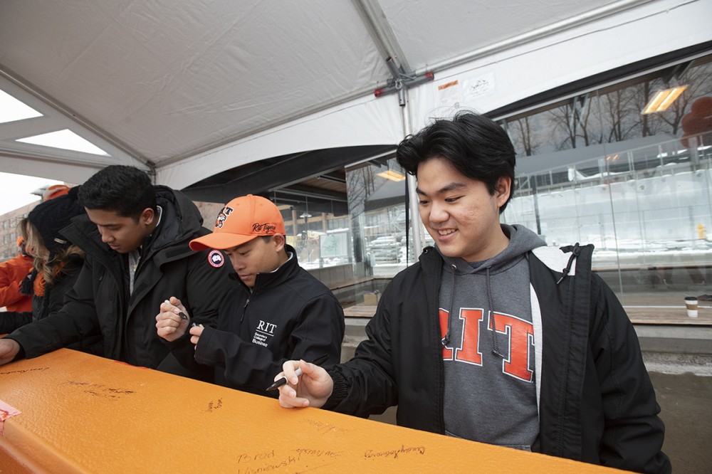 Photo by A. Sue Weisler <br> <p>RIT student Jonathan Dharmadi, right, is one of the first students to sign the SHED beam at a Jan. 12 event. He won the contest to name the makerspace and performing arts center. He is joined by&nbsp;Student Government President Lucas Randrianarivelo, left, and&nbsp;Student Government Vice President Christopher Ferrari.&nbsp;Their masks were briefly removed for the photo.</p>
