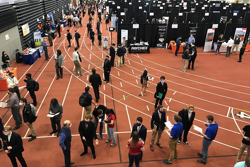 numerous students meeting with company reps at a career fair in a field house.