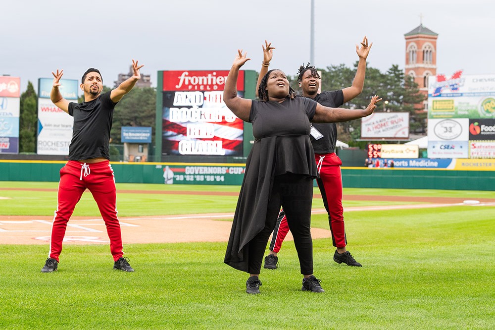 three people using American Sign Language on a baseball field.
