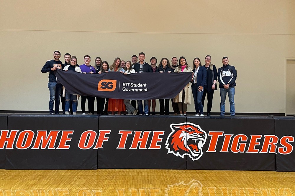 a group of student leaders standing on a stage in a gym.