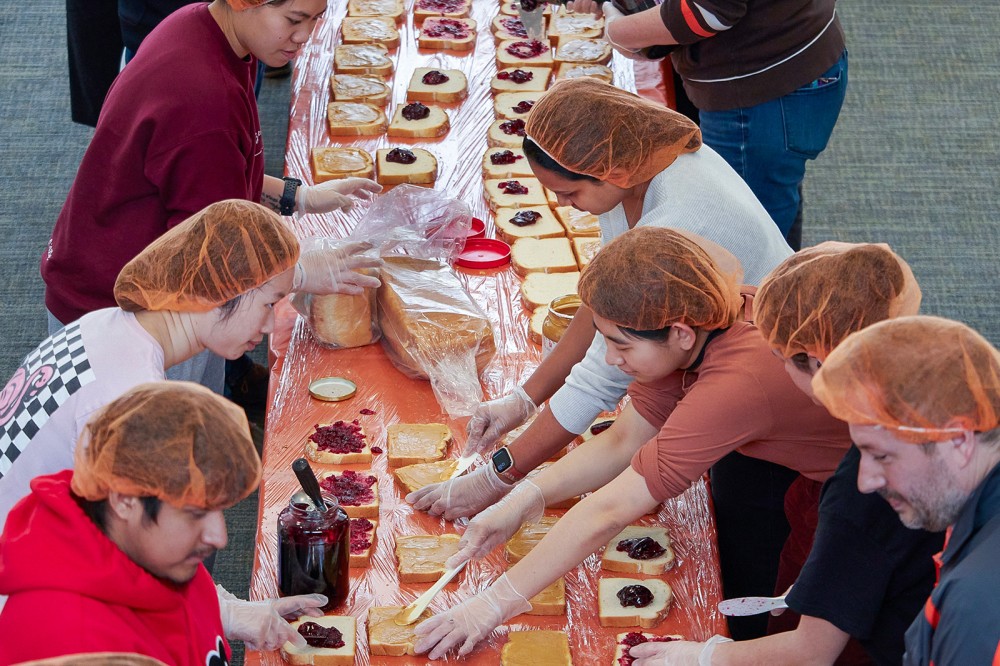 volunteers lined up on either side of a long table making peanut butter and jelly sandwiches.