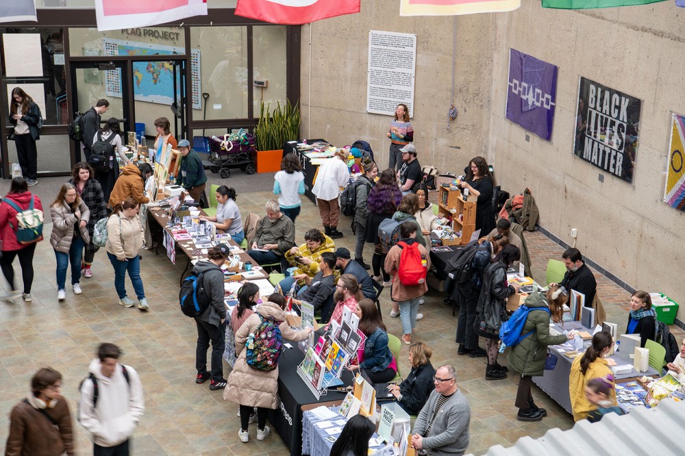 crowd of people in a building lobby looking at tables with craft items.