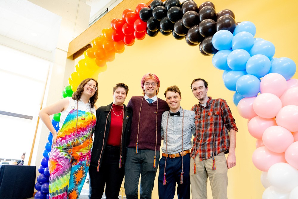 five college students standing under a balloon arch.