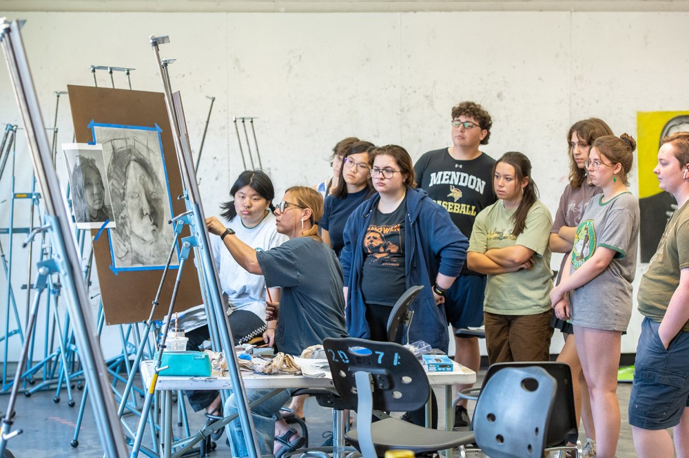 group of high school students watching a college professor draw on an easel.