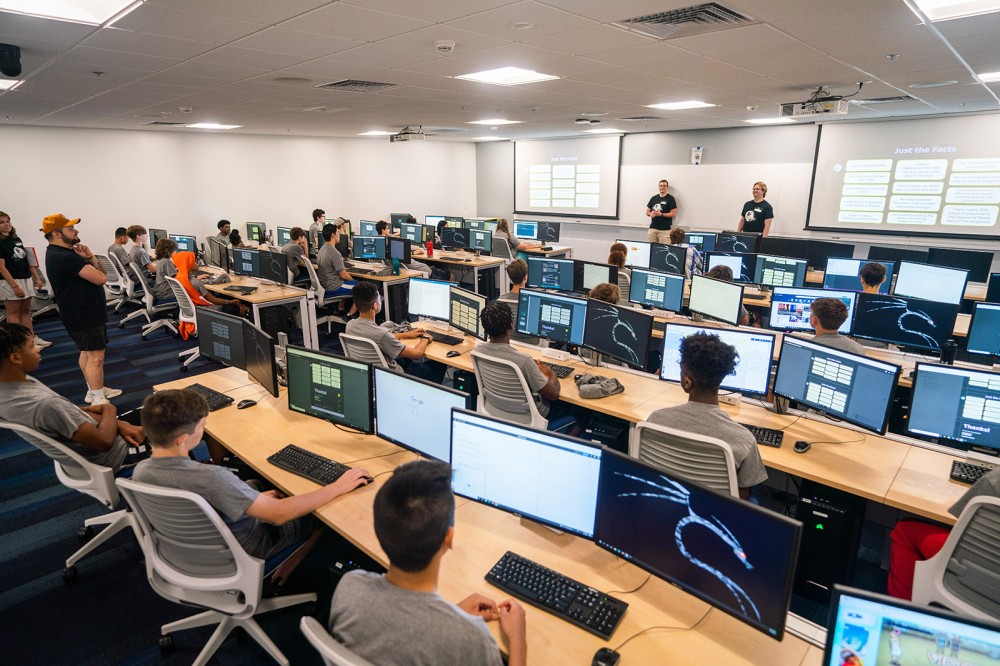 high school students sitting at rows of tables in a computer lab.