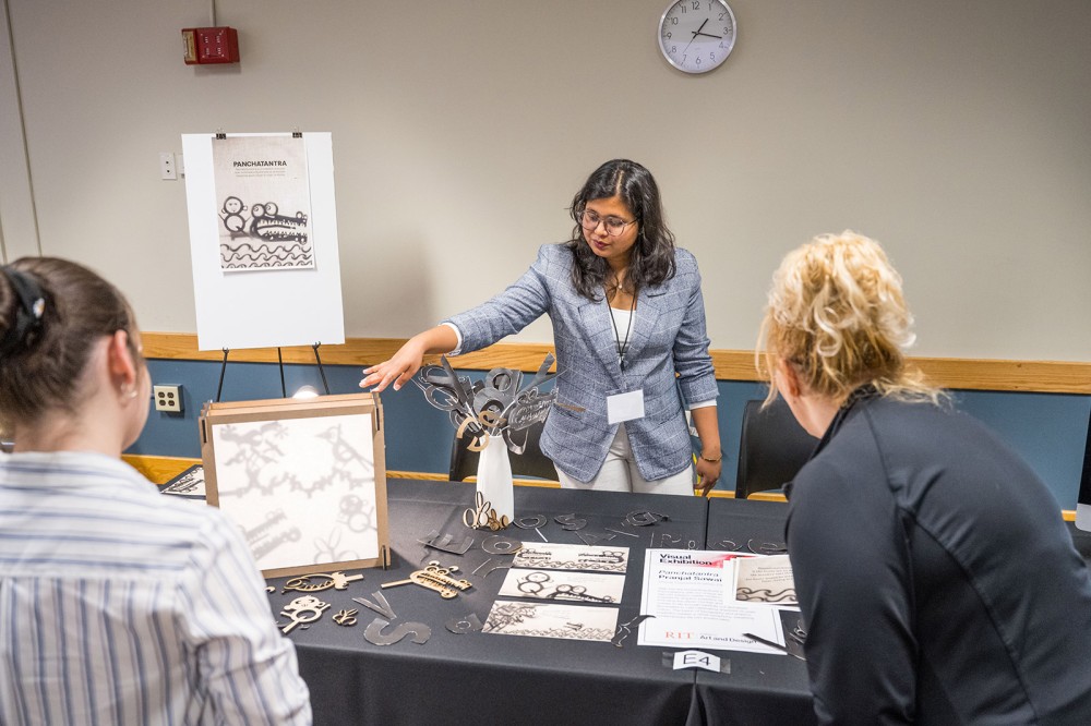 Pranjal Sawai is shown explaining her work to two people standing in front of her table.