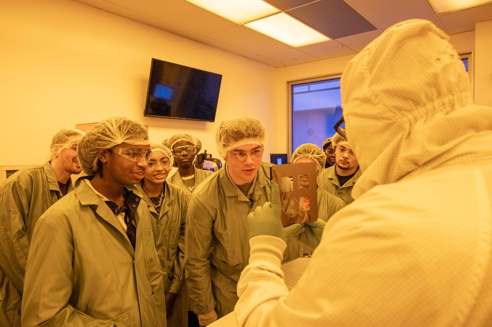 students face a professor in a clean room environment wearing suits that cover their whole body.