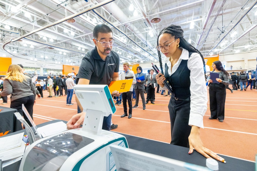 a man points to a screen while a younger college age female looks on.