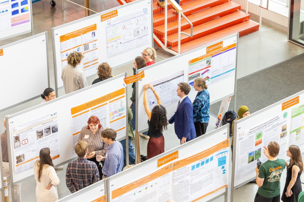 People stand around bulletin boards covered with research posters.