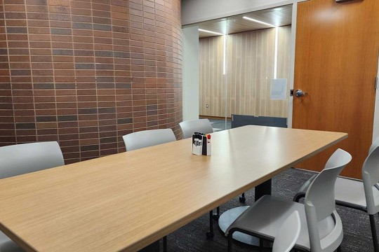 a meeting room with a table and six chairs, and a brick wall.