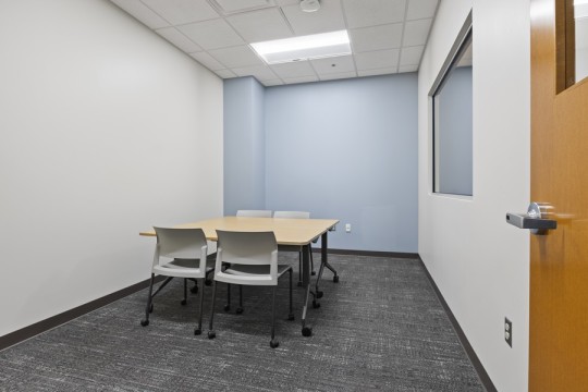 a small room with a two-way mirror, small table and four chairs.