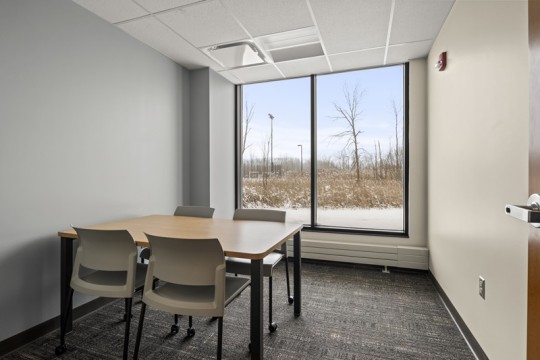 a meeting room with a table and four chairs, and a large window.