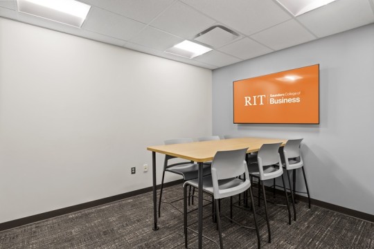 a meeting room with a table and six chairs, and a large T V on the wall.