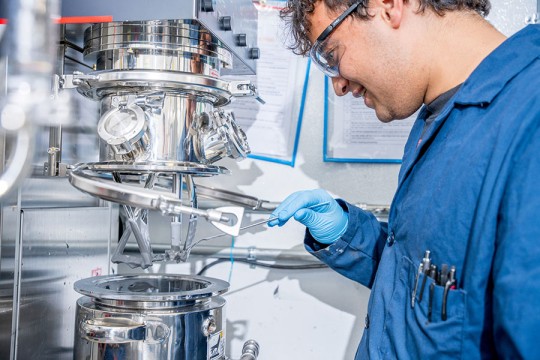 A student wearing a blue lab coat and working with a machine in the R I T Battery Development Center