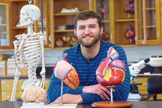 Student sits in lab with models of brain, heart and human skeleton