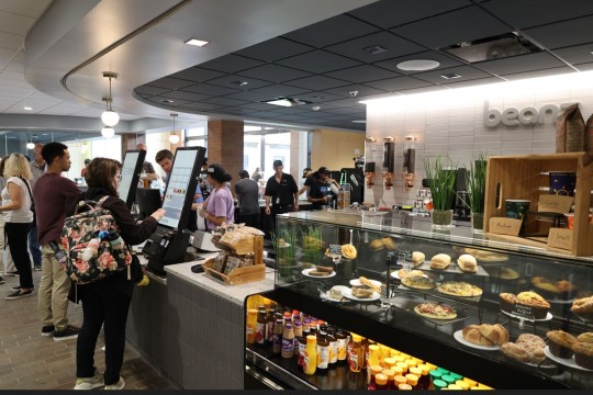 people in front of ordering kiosks on top of counters at Beanz cafe with treats displayed 