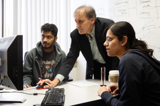 3 people looking at a computer monitor with a whiteboard in the background