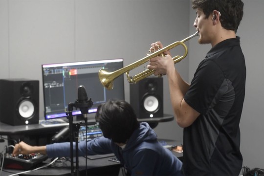 Daniel Sarch plays the trumpet as a fellow student edits on a computer.