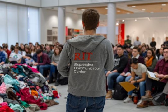 a photo of a male student speaking in front of a large group