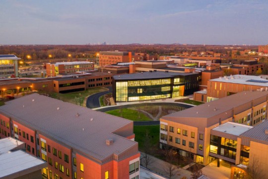 drone shot of the ESL Global Cybersecurity Institute, a black building with lit up windows surrounded by brick buildings on RIT campus.
