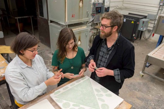 A group of people reviewing kilned glass around a workbench