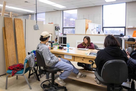 A group of students review a piece of work around a workbench